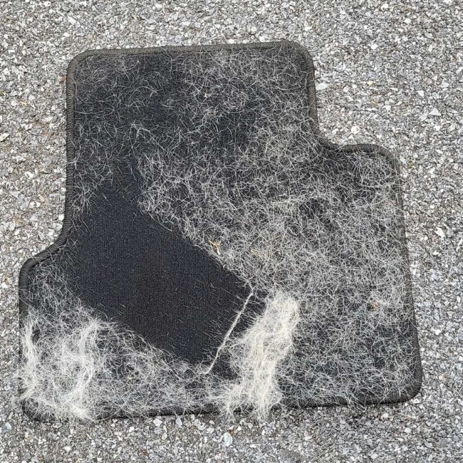 Car mat outdoors covered in stubborn embedded dog hair before cleaning